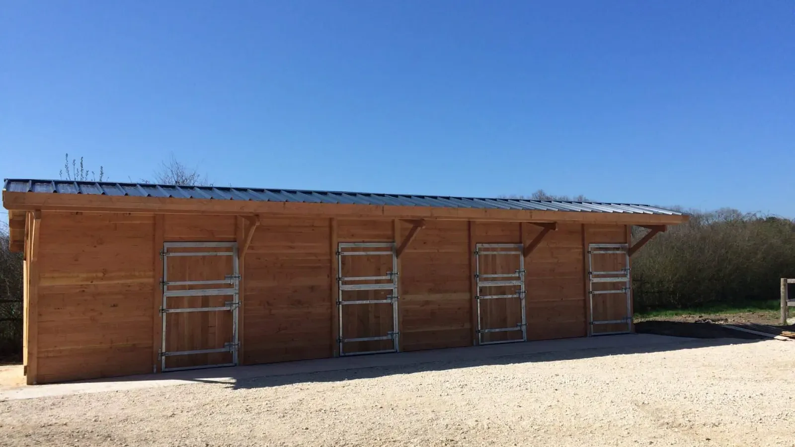 Barn en bois avec plusieurs boxes ouverts sur une cour gravillonnée